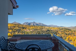 Un balcon avec une table et des chaises, donnant sur un paysage montagneux aux couleurs automnales.