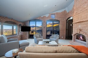 A modern living room with a stone wall, a fireplace, and a large window offering a mountain view.
