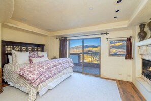 A bedroom with a large bed, a fireplace, and a view of mountains through a sliding glass door.