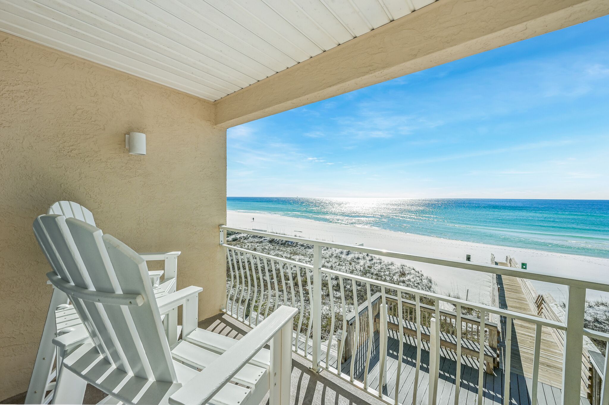 A balcony with white chairs and a view of a beach.
