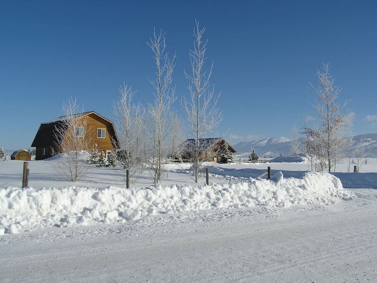 A snow-covered landscape with a wooden house and a clear blue sky.