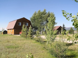 A wooden cabin with a sloped roof, surrounded by a grassy field and trees.