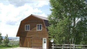A wooden barn with a large door and two windows, surrounded by a gravel driveway and a wooden fence. - 2BR Pet Friendly Darby Barn (Driggs)