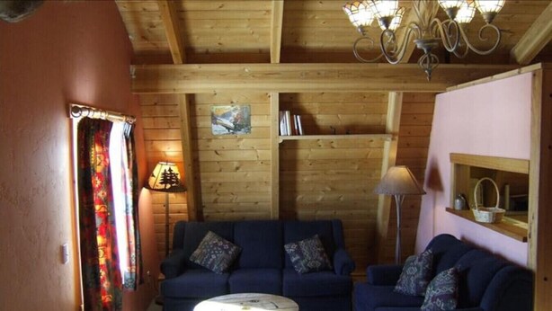 A cozy room with a wooden ceiling, a blue sofa set, a small round table, and a lamp. - 2BR Pet Friendly Darby Barn (Driggs)
