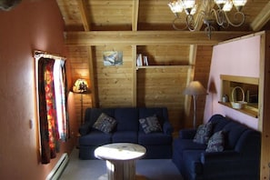 Ein gemütliches Zimmer mit Holzboden, einem blauen Sofagarnitur, einem kleinen runden Tisch und einer Lampe.
