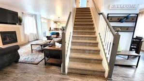 A staircase with a wooden finish, a living room with a fireplace, a television, and a 'WELCOME' sign. - 5 Minute Drive to Downtown Bend, Dog Friendly (Bend)
