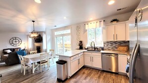 A modern kitchen with white cabinets, a stainless steel refrigerator, and a dining area with a table and chairs. - 5 Minute Drive to Downtown Bend, Dog Friendly (Bend)