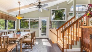 A dining area with a wooden table and chairs, a ceiling fan, and large windows with blinds.