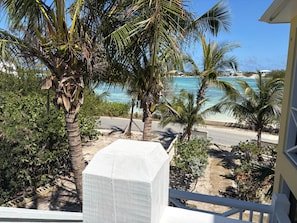 A balcony with a view of a beach, palm trees, and a clear sky.