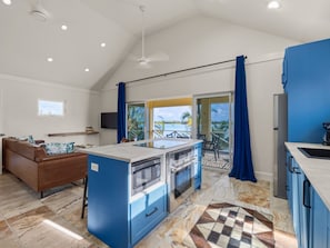 A kitchen with a central island, a dining area with a brown sofa, and a view of the outdoors.