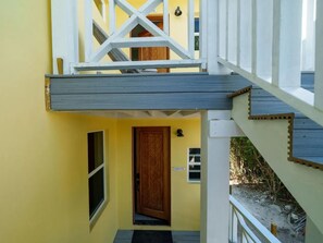 A yellow building with a wooden door, a window, and a staircase with white railings.