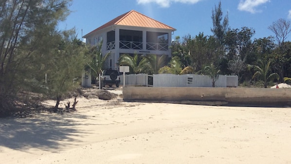 A two-story building with a red roof, surrounded by trees and a sandy area.