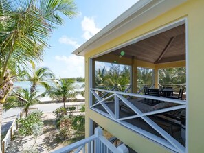 A covered outdoor seating area with a view of the beach and palm trees.