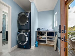 A laundry room with stacked washers and dryers, a shelf with folded towels, and a door leading to an outdoor area.