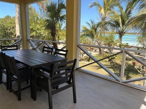 A covered outdoor dining area with a table and chairs, a view of palm trees and a beach.