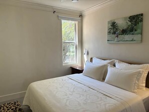 A bedroom with a bed, a window, a nightstand, and a painting on the wall.