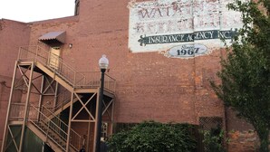 Un edificio de ladrillo con un gran mural que anuncia una agencia de seguros, una escalera metálica y un farol.