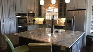 Une cuisine moderne avec des meubles blancs, des appareils en acier inoxydable, un îlot en granit et des luminaires suspendus.