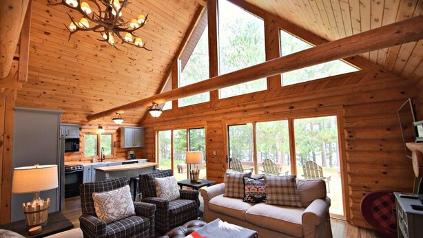 L’intérieur d’une cabane en rondins comprend une cuisine, un coin repas et un espace détente, le tout baigné de lumière grâce à de grandes fenêtres.