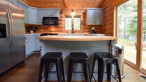 Une cuisine moderne avec un plafond en bois, des armoires grises, un réfrigérateur en acier inoxydable, un four à micro-ondes et une grande fenêtre donnant sur l’extérieur.