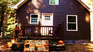 A wooden cabin with a welcoming sign, a porch, and a stone foundation. - "Your Neck of the Woods" Cabin Rental: Peaceful Get-away Overlooking Fish Creek (Taberg)