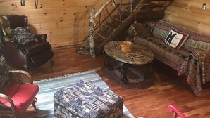 A cozy cabin interior with a wooden interior, a sofa, a chair, a small table, and a staircase. - "Your Neck of the Woods" Cabin Rental: Peaceful Get-away Overlooking Fish Creek (Taberg)
