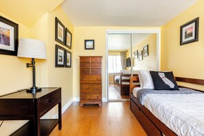 A bedroom with a bed, dresser, lamp, and a view into another room.