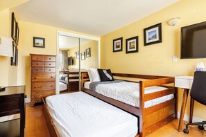 Une chambre d’hôtel avec un lit en bois, une commode, un bureau et une chaise. Les murs sont ornés de tableaux encadrés et il y a une télévision.