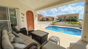 Zona junto a la piscina con mobiliario de mimbre, una piscina pequeña y vistas de edificios cercanos.