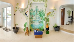 Ein Zimmer mit einer Dschungel-Muralmalerei, einem großen Fenster und einem Essbereich mit Stühlen und Tisch.