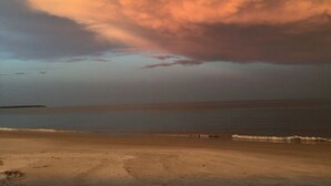 A beach with a wide sandy shore and a calm sea under a cloudy sky.
