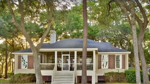 A two-story house with a porch, surrounded by trees.