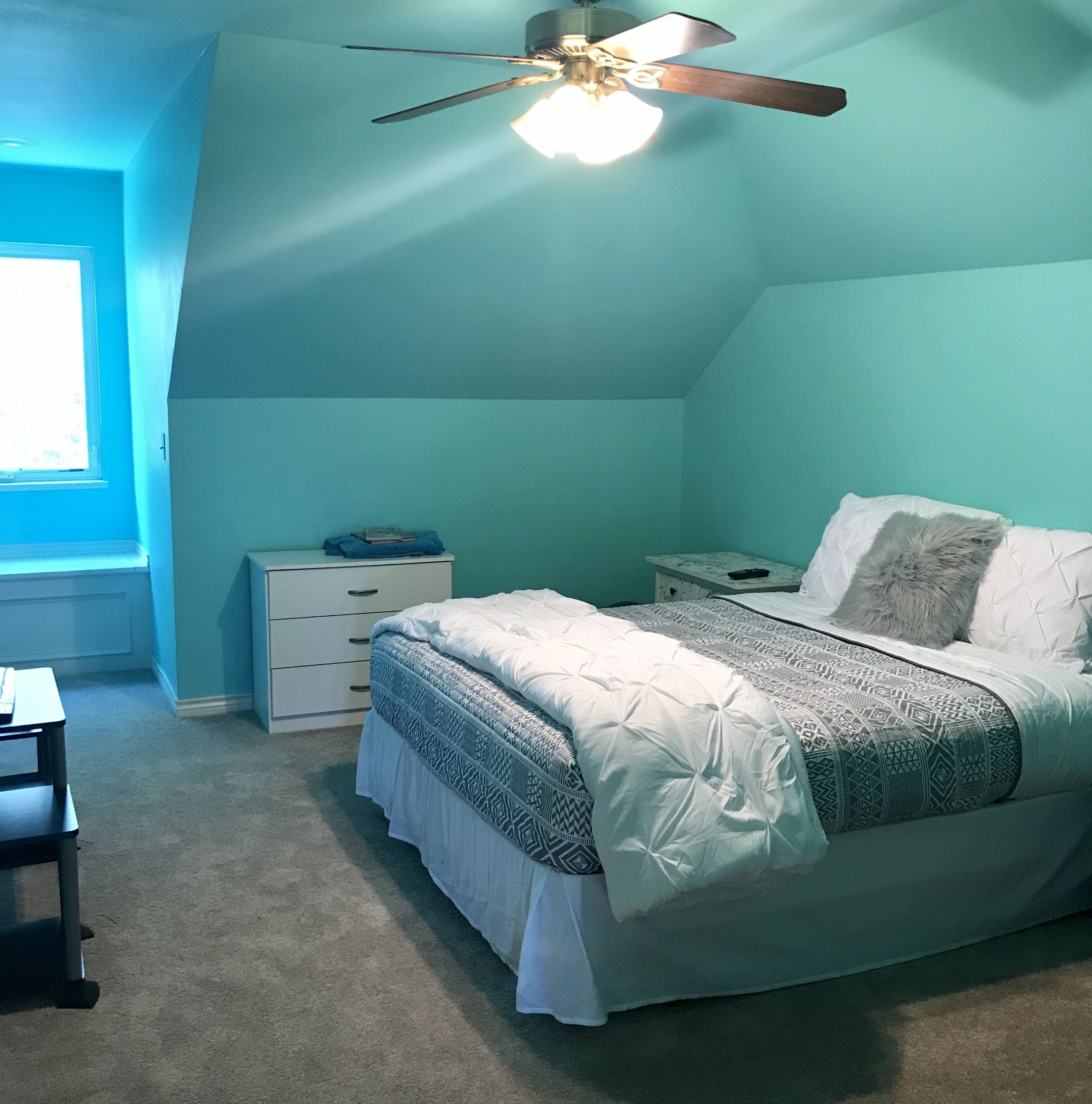 A bedroom with a bed, a nightstand, a desk, and a window.