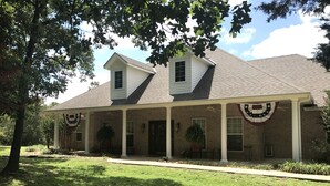 A two-story house with a covered porch, brick exterior, and American flags. - Gorgeous Home In Upscale Neighborhood - Room For The Whole Family 4 bedrooms! (Pawhuska)