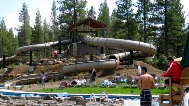 Un parc aquatique doté d’un grand toboggan aquatique, d’un espace piscine avec des chaises longues et d’une terrasse en bois.