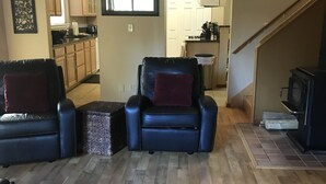 Un salon avec deux fauteuils en cuir, un tapis à motifs et une vue sur la cuisine.