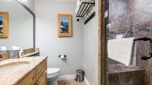Un baño con encimera de granito, inodoro, ducha con puerta de vidrio y un perchero para toallas.