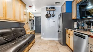 Una cocina con armarios de madera, un refrigerador de acero inoxidable, un lavavajillas y un sofá de cuero negro.