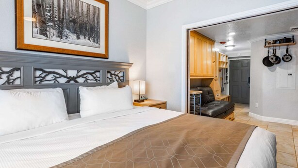 Habitación de hotel con una cama grande, una mesita de noche, un cuadro en la pared y vistas al área de la cocina.