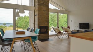 A modern living room with a fireplace, large windows, and a dining area with chairs and a table.