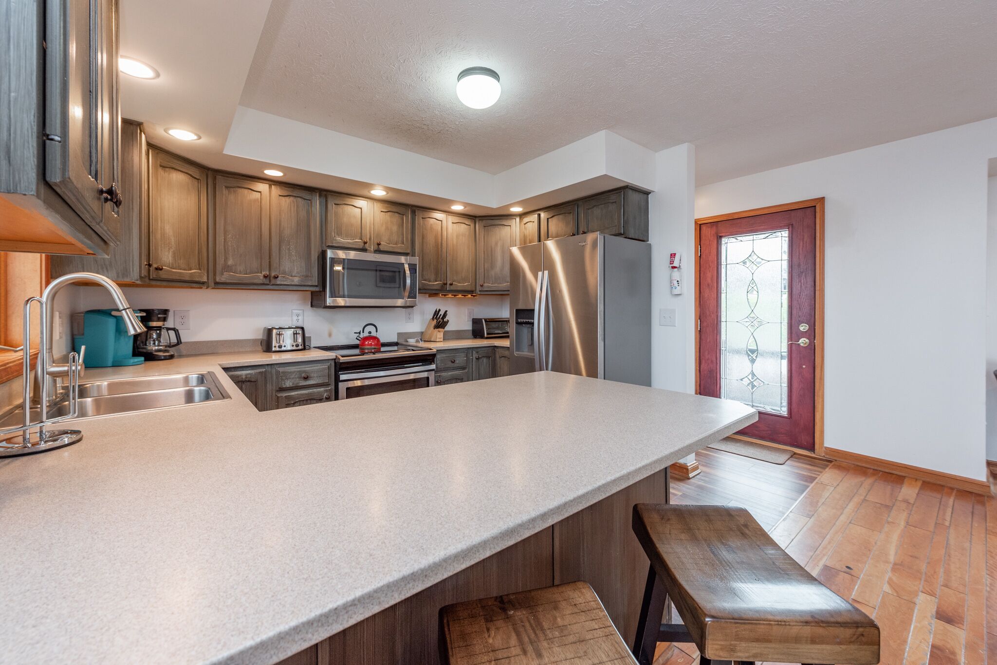 A modern kitchen with wooden cabinets, stainless steel appliances, a large island, and a bench.