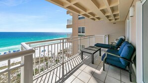 Un balcon avec vue sur la plage et l’océan. On y trouve deux chaises et une petite table.