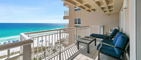 A balcony with a view of the beach and ocean. There are two chairs and a small table.