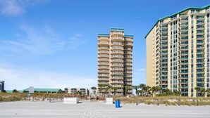 Un hôtel en bord de mer doté de nombreux balcons, une plage de sable en premier plan et un ciel bleu dégagé.