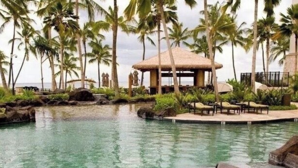 Un espace piscine doté de chaises longues et d’un kiosque entouré de palmiers.