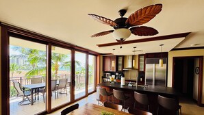 Une cuisine spacieuse dotée d’un grand îlot central, d’appareils électroménagers modernes et offrant une vue sur un espace extérieur de style tropical.