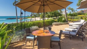 Une terrasse au bord de la plage, avec une table ronde, des chaises et un grand parasol.