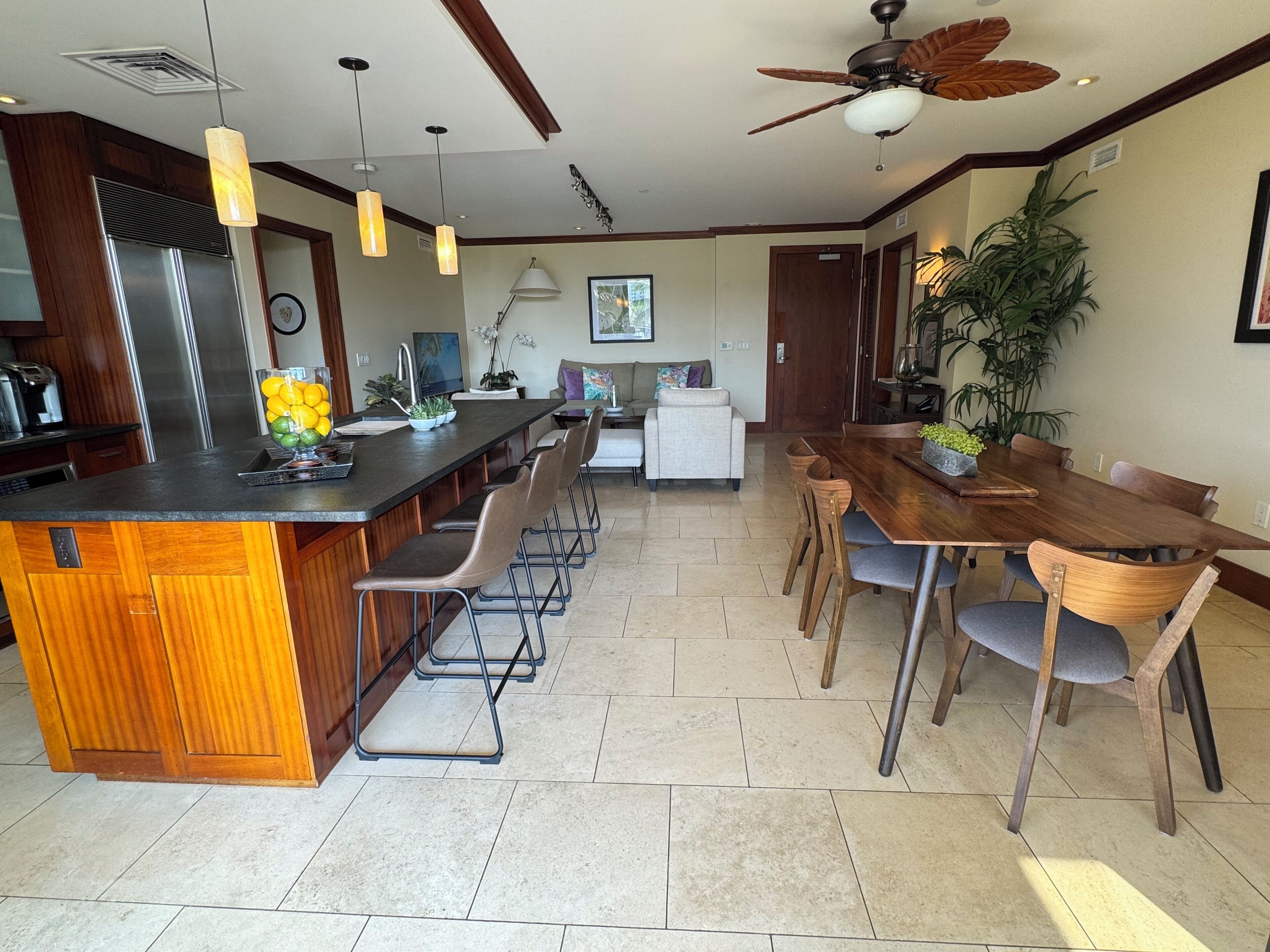 A spacious kitchen with a central island, a dining area with a wooden table and chairs, and a ceiling fan.