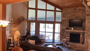 A cozy living room with a stone fireplace, leather sofa, and a television mounted on the wall. - Deer Valley-100yds~1min walk. Closest Powder Run Penthouse. Deck Hot Tub w'Views (Park City)