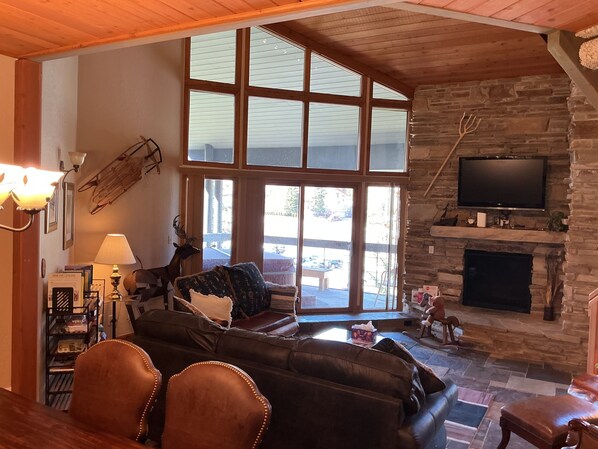 A cozy living room with a stone fireplace, leather sofa, and a television mounted on the wall.